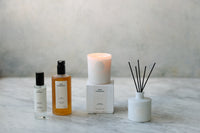 Set of home fragrance products including a candle, diffuser, and bottles on a marble surface.