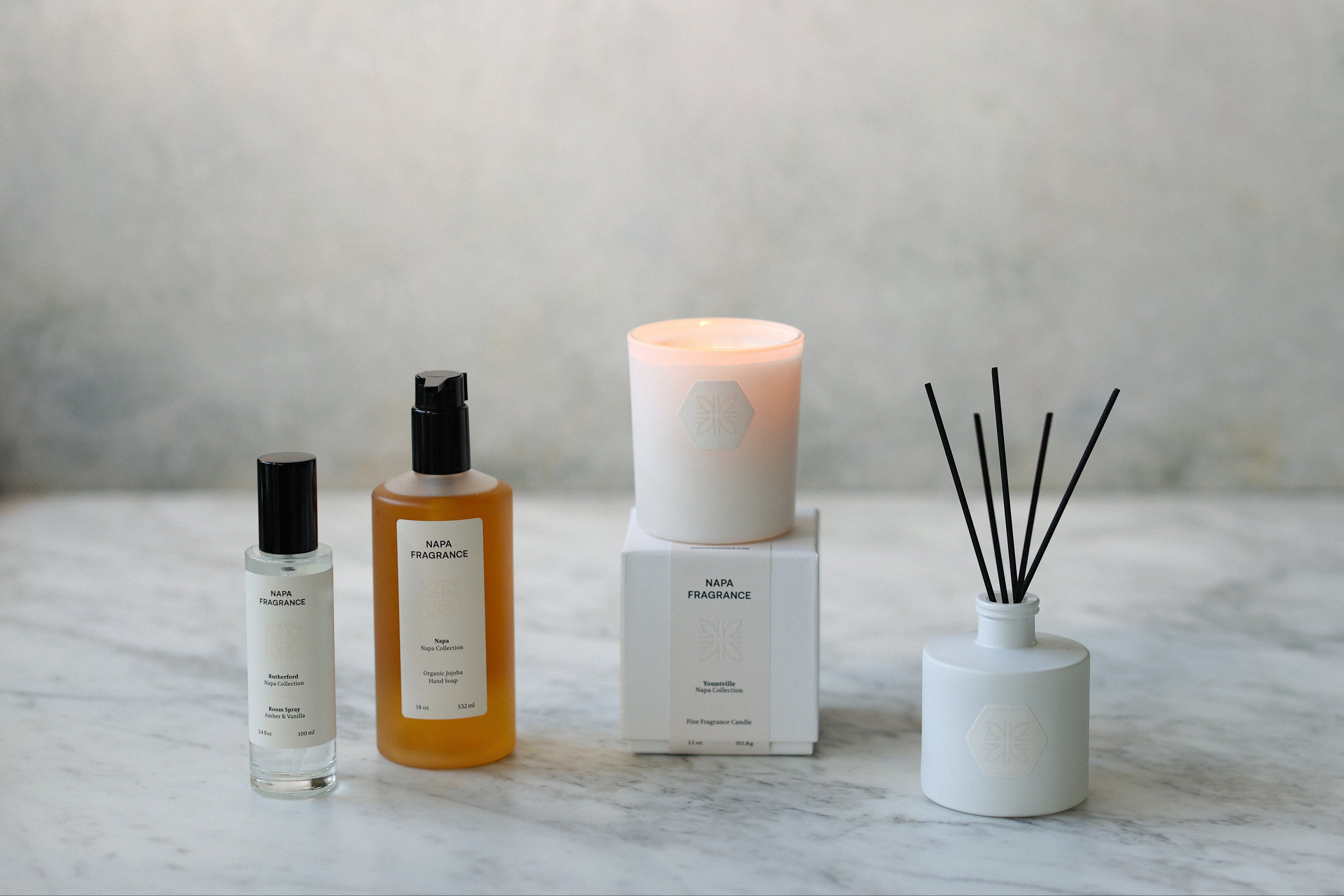 Set of home fragrance products including a candle, diffuser, and bottles on a marble surface.