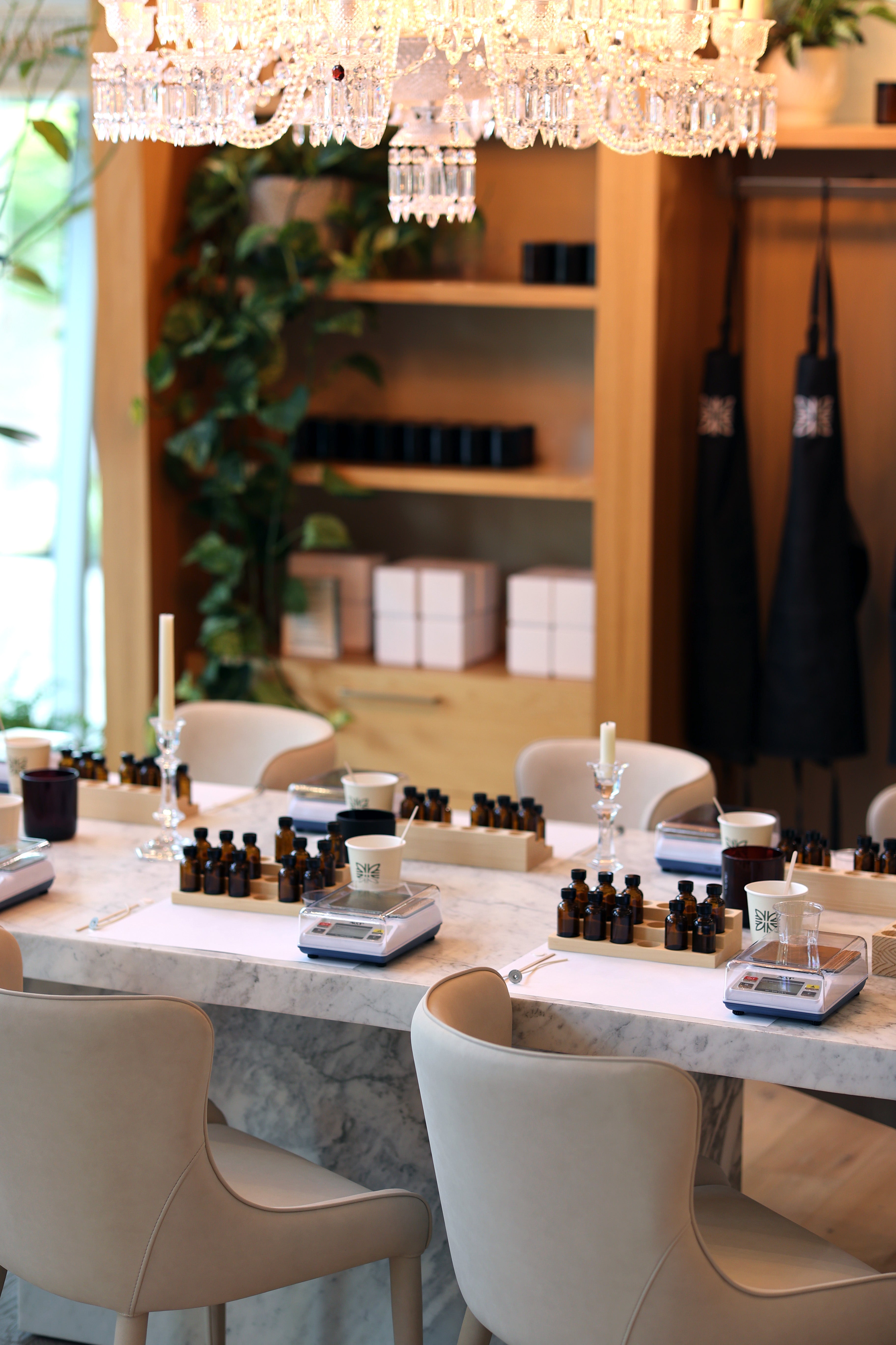 Studio with tables, chairs, and fragrance bottles under a chandelier.
