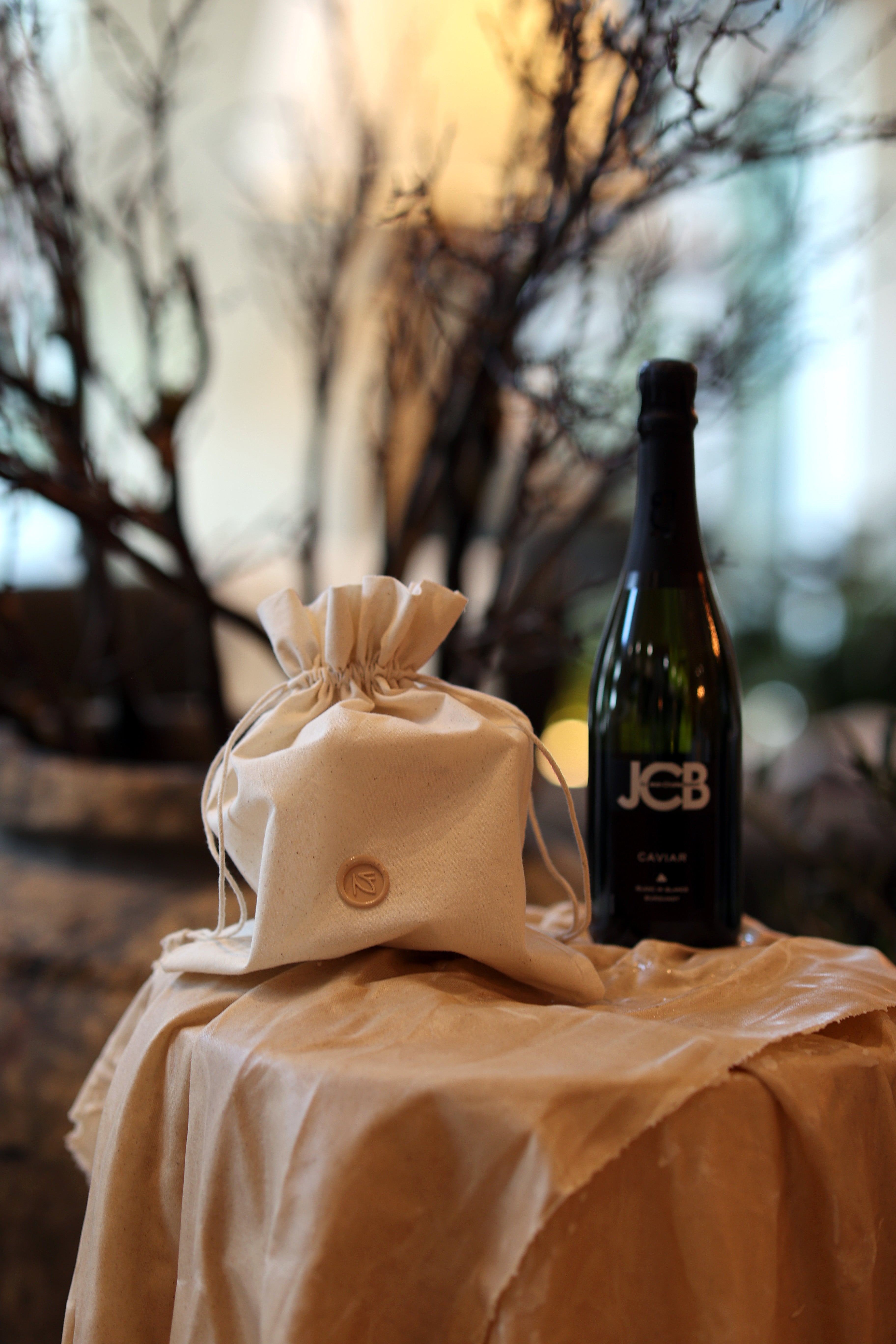 Bottle of JCB wine with a drawstring bag on a table outdoors.