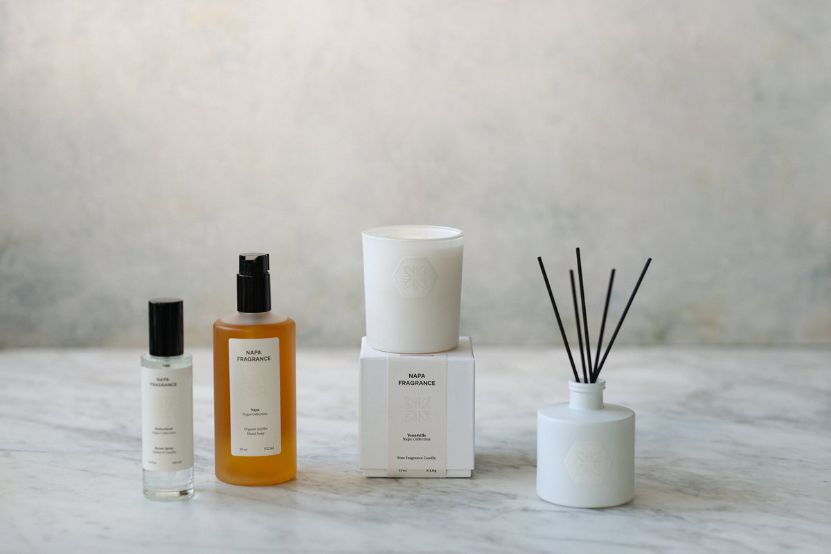 Set of home fragrance products including bottles, a candle, and diffuser on a marble surface.