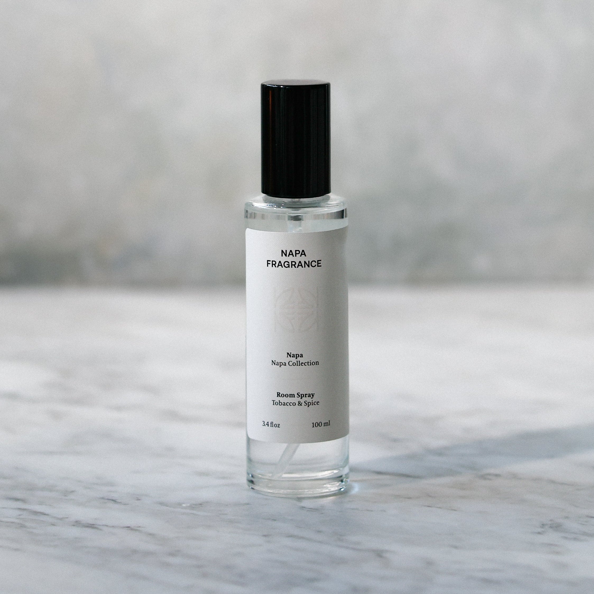 Small clear bottle with black cap on a marble surface with a blurred gray background