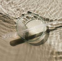 Clear glass pipette with a glass dish on a reflective water surface