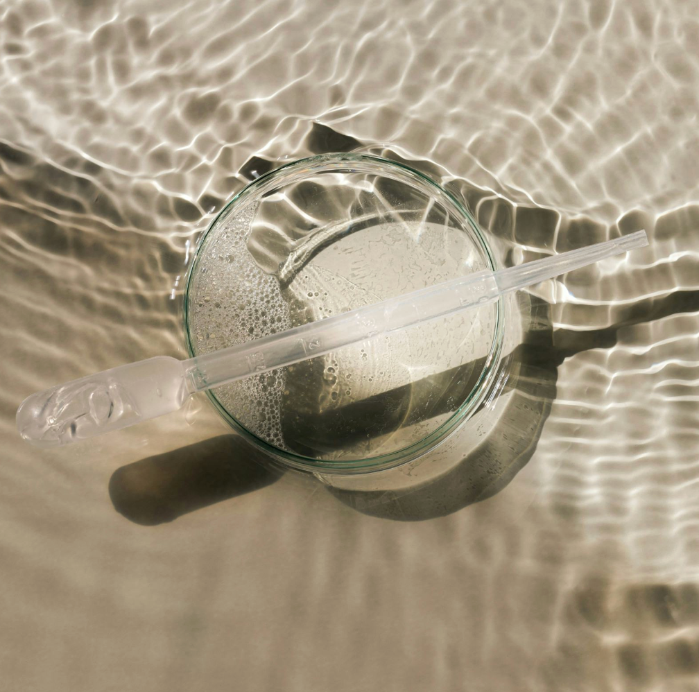 Clear glass pipette with a glass dish on a reflective water surface